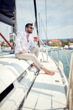 Genç bir adam güzel güneşli bir denizde yatta otururken kahvenin tadını çıkarıyor. Yaz, deniz, tatil