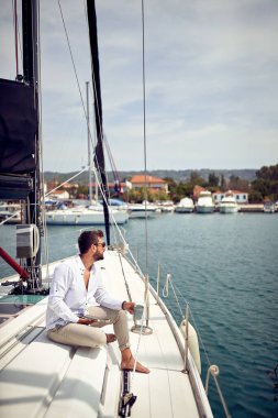 Genç bir adam denizde bir yatta oturmuş güneşli bir günde tablet kullanırken manzaranın tadını çıkarıyor. Yaz, deniz, tatil
