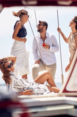 Bir grup düşünceli genç ve yakışıklı model, deniz kenarında güzel bir günde yatın güvertesinde fotoğraf çektirirken güneşte harika vakit geçiriyorlar. Yaz, deniz, tatil, arkadaşlık