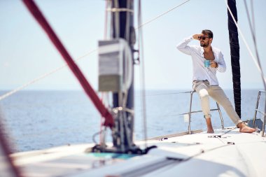 Genç ve yakışıklı bir erkek model, deniz kenarında güneşli bir günde yatta çekilmiş bir fotoğraf çekiminin tadını çıkarıyor. Yaz, deniz, tatil