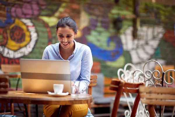在酒吧花园的一个美丽的日子里 一位年轻的女学生一边享受着在笔记本电脑上工作的乐趣 一边喝咖啡 — 图库照片