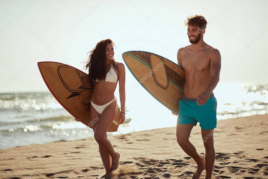 Young couple of surfers is walking the beach at a beautiful day at sea. Summer, vacation, sea, together