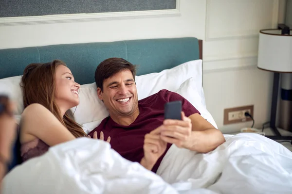 Jovem Casal Caucasiano Desfrutando Cama Juntos Rindo Olhando Para Telefone — Fotografia de Stock