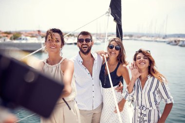 Bir grup genç ve yakışıklı manken, deniz kenarında güzel bir yaz günü rıhtımda at sürerken yatın güvertesinde fotoğraf için poz veriyorlar. Yaz, deniz, tatil, arkadaşlık