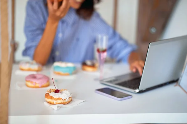 Uma Mulher Está Comendo Deliciosos Donuts Enquanto Senta Usa Laptop — Fotografia de Stock