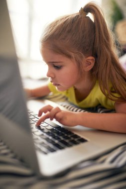 Evde rahat bir atmosferde dizüstü bilgisayarda yazan küçük bir kız. Oyun, çocukluk, ev
