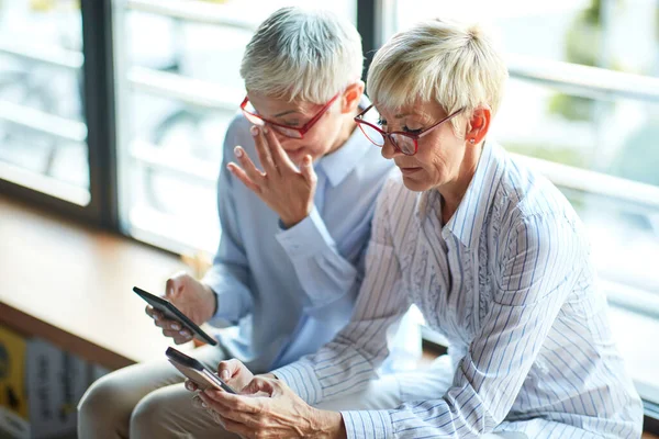 Två Äldre Affärskvinnor Med Liknande Utseende Använder Smartphones Pausen Avslappnad — Stockfoto