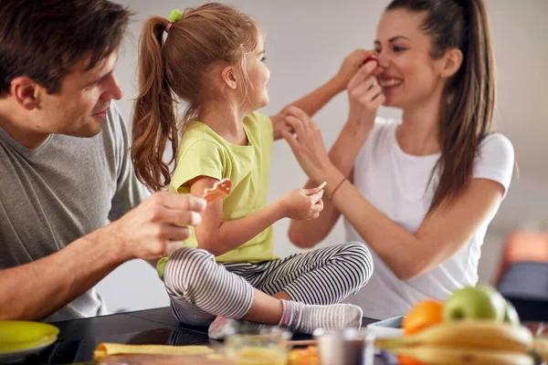 一緒に家で明るい雰囲気の中で朝食を食べながら楽しい時間を過ごしている若い家族 一緒に — ストック写真