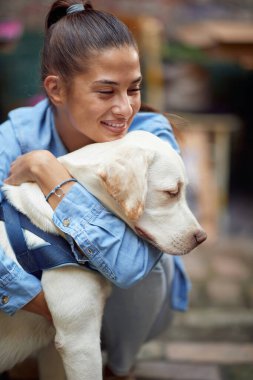 Güzel, genç, beyaz bir kadın köpeğini gözleri kapalı kucaklıyor, gülümsüyor.