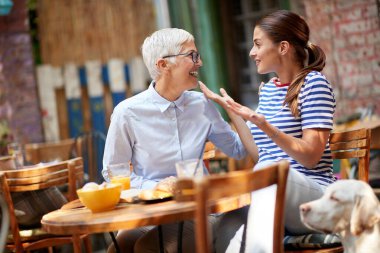 Yetişkin kız ve anne ilişkisi kavramı. Genç ve güzel bir esmer, son sınıf öğrencisiyle konuşuyor, açık kafede kahve içiyor, gülümsüyor.