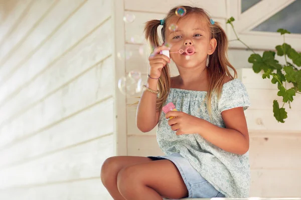 可爱可爱可爱的高加索小女孩坐在门廊上 制造肥皂泡 — 图库照片