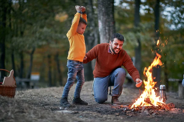 美しい秋の夕暮れに森の中でキャンプファイヤーのために興奮した父と息子 — ストック写真