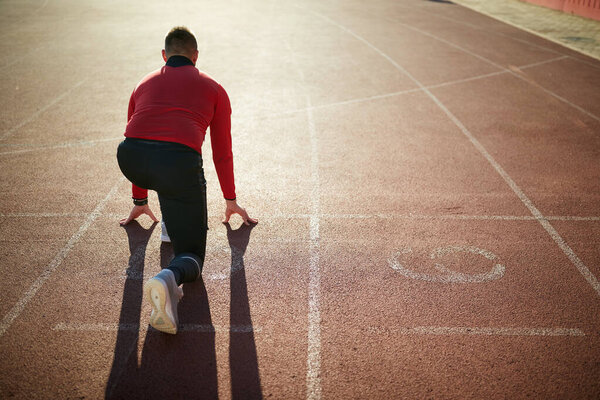 Young man sprinters at starting position ready for race on racetrack.