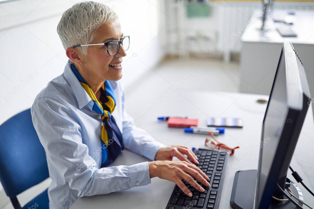 A female professor in front of a computer desk at the informatics lecture in the university computer classroom. Professor working at the college. Education, college, university, learning and people concept