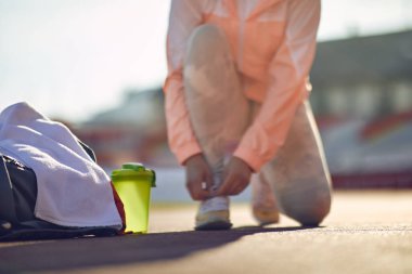 Ayrıntılar, beyaz kadın görüntüsü stadyumda diz çökmüş, ayakkabı bağcıklarını bağlıyor, eğitime hazırlanıyor.