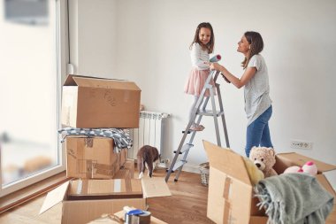 Genç anne kızıyla eğleniyor merdivende dikiliyor, duvarı boyamaya hazırlanıyor.