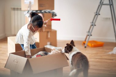 Köpekli küçük bir kız, ailesinin yeni taşındığı evin hoş atmosferinde eşyaları yerleştiriyor. Ev, aile, taşınma.