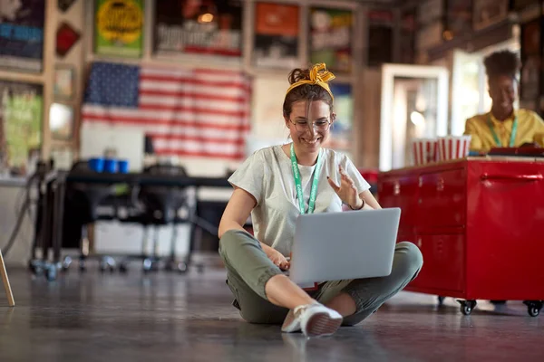 若いクリエイティブの女性が床に座ってオフィスの明るい雰囲気の中で働いている間に楽しんでいます 従業員 オフィス — ストック写真