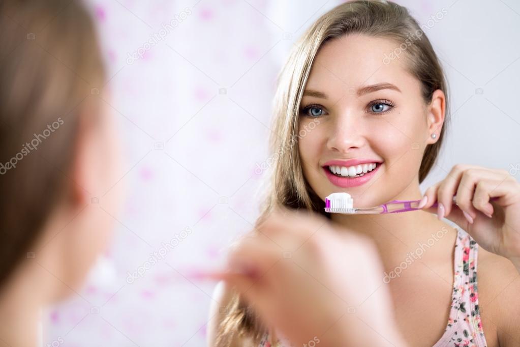 Pretty female looking in mirror while brushing teeth