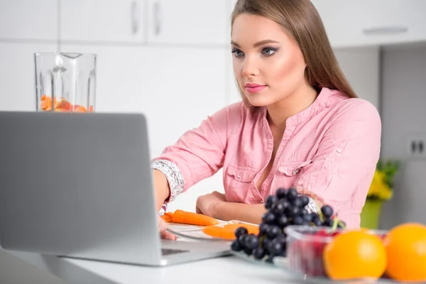 Mujer cocinera mirando el ordenador portátil mientras se prepara la comida en la cocina —  Fotos de Stock