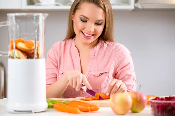 Smiling young woman cutting carrot — Stock Photo, Image