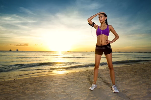 Sporty woman standing by the ocean beach at sunset — ストック写真