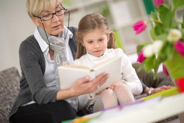 Girl interested looks at the book while grandma  read — Stockfoto