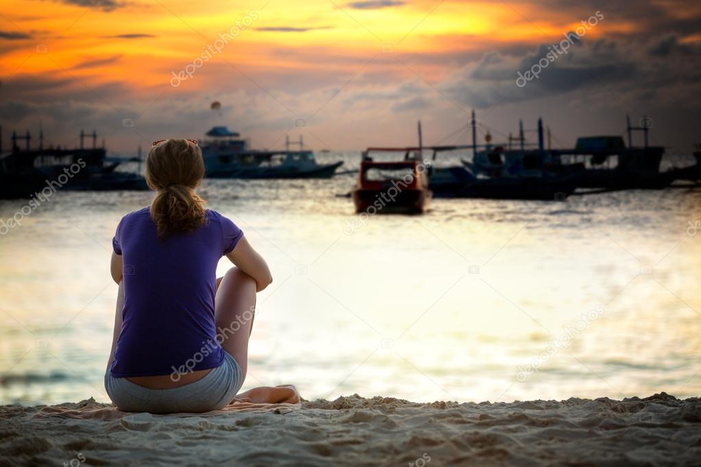 Woman sitting on sea cost and looking in beautiful sunset