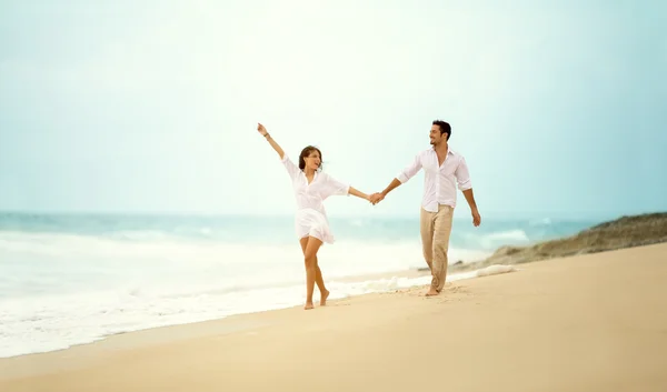 Směje se pár v lásce drží ruku na pláži — Stock fotografie