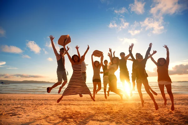 Jovens felizes pulando na praia no belo pôr do sol — Fotografia de Stock