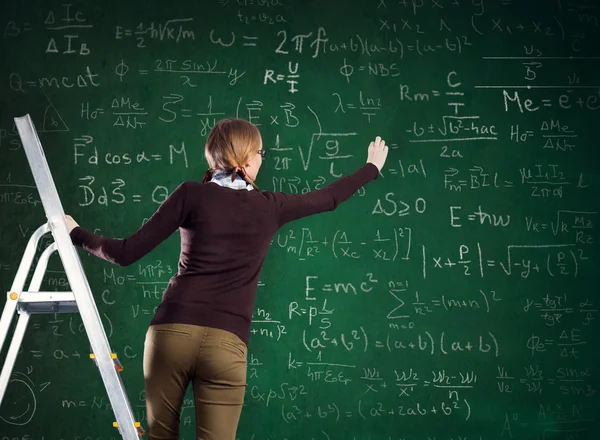 Student on a ladder and writes on a chalkboard — Stock Photo, Image