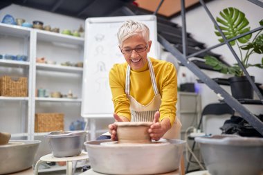 Yaşlı, gülümseyen bir kadın çömlekçilikten zevk alıyor. Yaratıcı, hobi, atölye konsepti