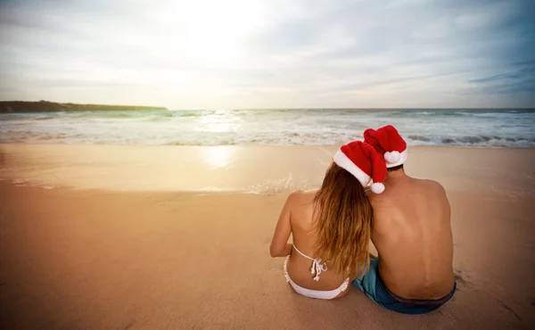 Couple avec chapeaux de Père Noël assis sur la plage de sable — Photo