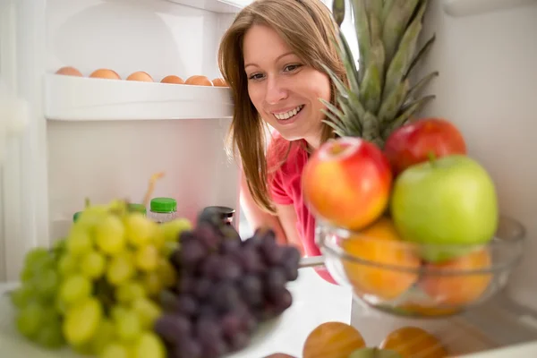 Femme souriante regarder les fruits au réfrigérateur — Photo