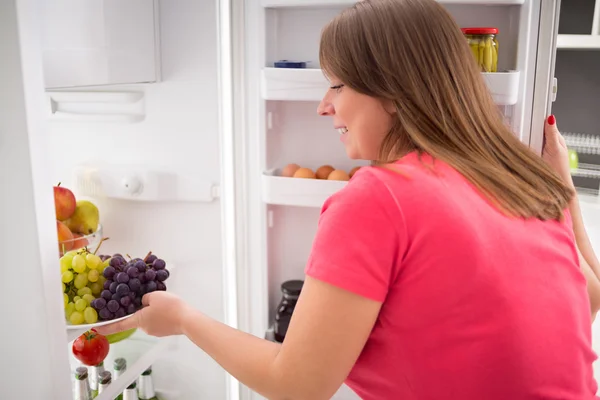 Hemmafru tar tallrik full av druvor från kylskåp — Stockfoto