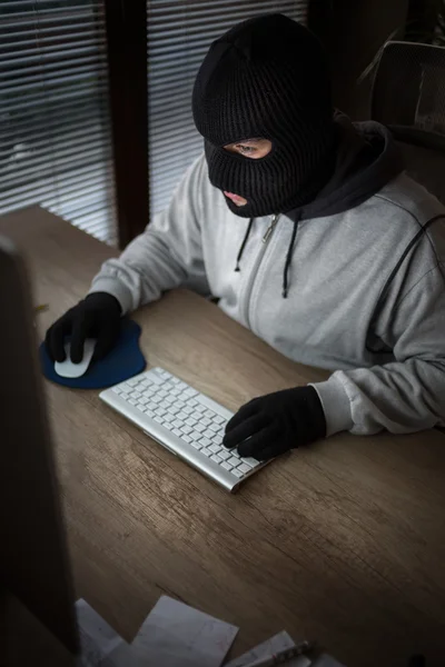 Ladrão mascarado sentado na frente do computador — Fotografia de Stock