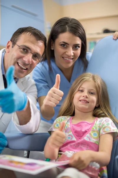 Giovane ragazza con dentista e il suo assistente spettacolo pollice in su e smil — Foto Stock