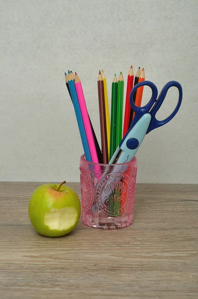 Un bicchiere pieno di matite coloranti e una forbice con una mela — Foto Stock