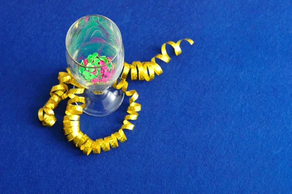 Confetti, uma fita presente e taça de champanhe exibida em um fundo azul — Fotografia de Stock