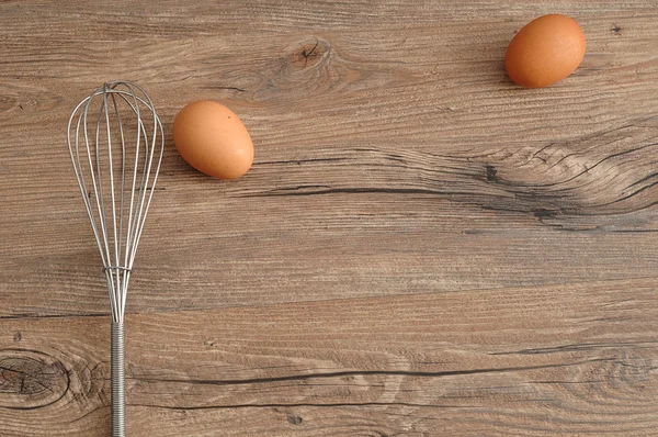 An egg beater, whisk, with two eggs