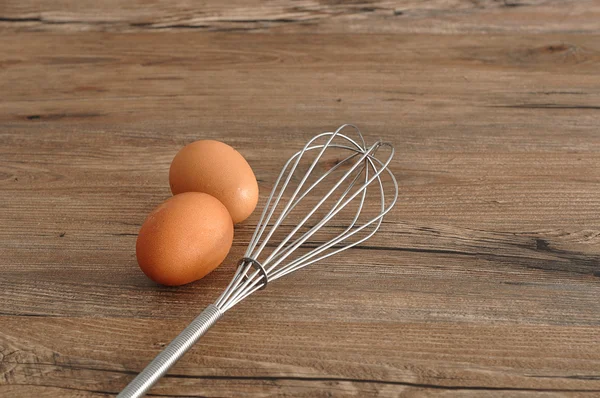 An egg beater, whisk, with two eggs