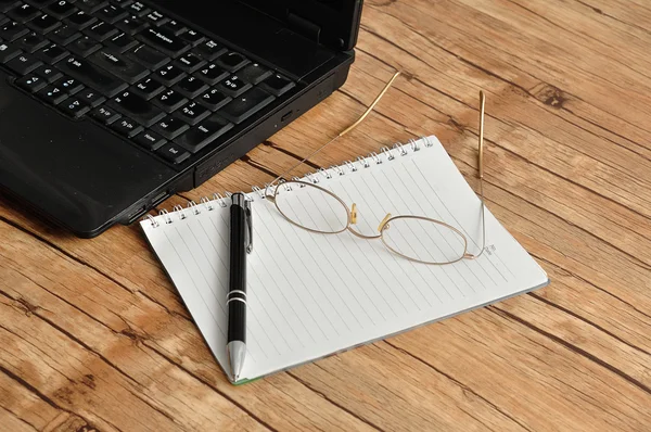 A laptop with reading glasses, a pen and a note book — Stock Photo, Image