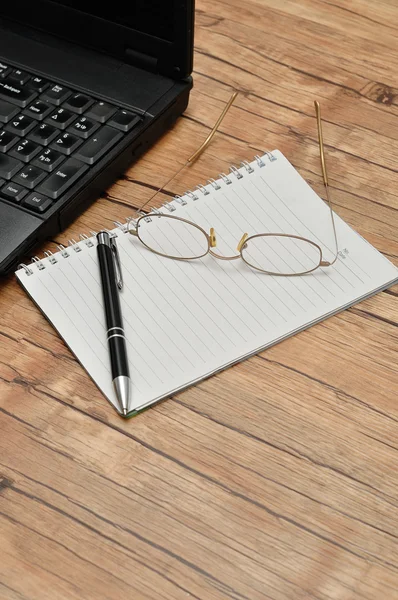 A laptop with reading glasses, a pen and a note book — Stock Photo, Image