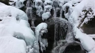Dağlarda kış şelalesi. Su kar ve buzu delip geçer.