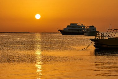 Denizde şafak vakti. Güneş suyun üstünde, yatın arka planında yükseliyor.