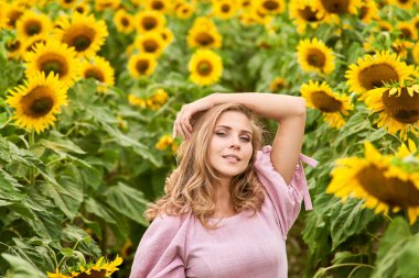 Genç ve güzel bir kız, ayçiçeklerinin arasında bir tarlada duruyor. Çiçek tarlasında yaz fotoğrafçılığı