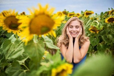 Sevimli hoş bir kadın gülümser ve kulaklarını kapatır. Kız büyük çiçeklerin arka planındaki hoş şeyleri düşünüyor. Seçici odak