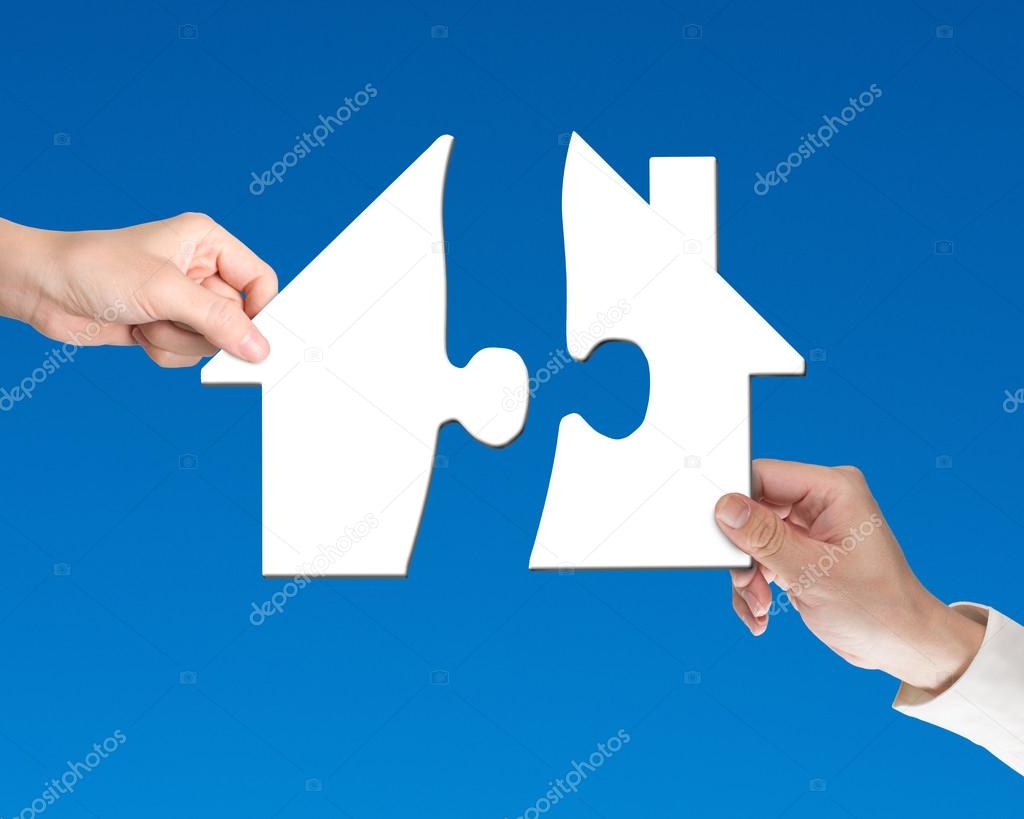 Two hands holding jigsaw pieces to finish house shape puzzle