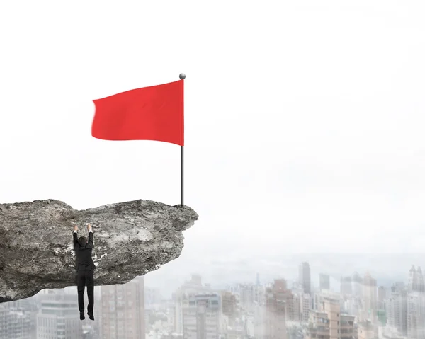 Хвилястий червоний прапор на вершині скелі з висячим бізнесменом — стокове фото