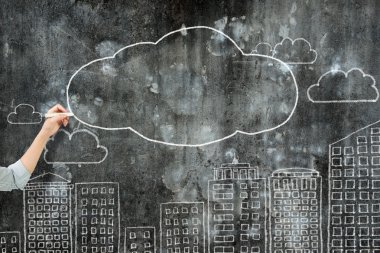 Woman hand holding chalk drawing clouds city buildings 